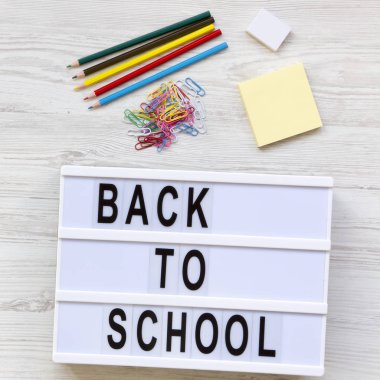 Eğitim kavramı. Silgi, kurşun kalem, çıkartmalar, ataç ve 'Back to school' kelime bir beyaz tahta yüzey üzerinde modern bir gemide. Yukarıdan, tepegöz, düz yatıyordu.