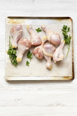 Pişmemiş tavuk budu fırın bir yaprak kağıt tepsisindeki, yüksek açılı görünüş üzerinde. Beyaz ahşap zemin.