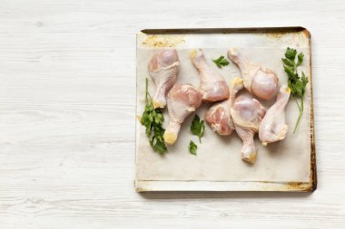 Çiğ çiğ tavuk pişirme bir yaprak kağıt tepsisindeki, yüksek açılı görünüş bacaklarına. Beyaz ahşap arka plan. Kopya alanı.