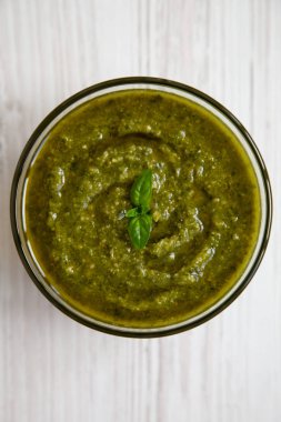 Taze fesleğen pesto Beyaz ahşap yüzeyde bir kasede yaptı, yukarıdan görüntüleyin. Düz yatıyordu, ek yükü.