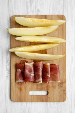 Beyaz ahşap arka plan üzerinde üstten görünüm kavun dilimleri ile prosciutto bambu üzerinde kurulu.