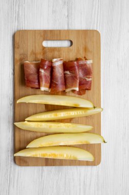 Kavun dilimleri ile prosciutto bambu üzerinde beyaz ahşap masa, üstten görünüm üzerinde kurulu. Tepegöz, lay, yukarıdan düz. Yakın çekim.