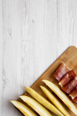 Kavun dilimleri ile prosciutto bambu üzerinde beyaz ahşap zemin, üstten görünüm üzerinde kurulu. Tepegöz, lay, yukarıdan düz. Metin için yer.