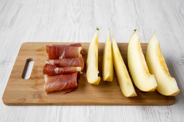 Kavun dilimleri ile prosciutto bambu üzerinde beyaz ahşap zemin, yan görünüm üzerinde kurulu. Portre.