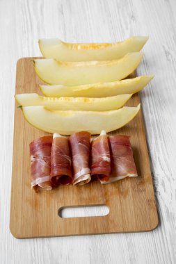 Beyaz ahşap yüzey üzerinde yüksek açılı görünüş kavun dilimleri ile prosciutto bambu üzerinde kurulu. 