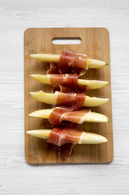 Kavun dilimleri üzerinden Beyaz ahşap yüzey, en iyi görünüm prosciutto Bambu tahta üzerinde sarılı. Yakın çekim. Yukarıda, ek yükü. 
