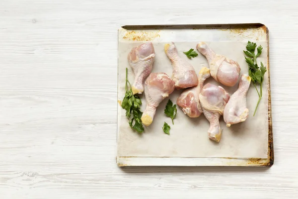 Çiğ çiğ tavuk pişirme bir yaprak kağıt tepsisindeki, yüksek açılı görünüş bacaklarına. Beyaz ahşap arka plan. Kopya alanı.