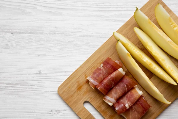 Kavun dilimleri ile prosciutto bambu üzerinde beyaz ahşap yüzey, üstten görünüm üzerinde kurulu. Tepegöz, lay, yukarıdan düz. Kopya alanı.