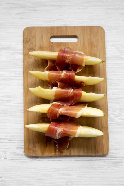 Kavun dilimleri üzerinden Beyaz ahşap yüzey, en iyi görünüm prosciutto Bambu tahta üzerinde sarılı. Yakın çekim. Yukarıda, ek yükü. 