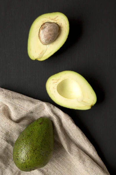 Aguacates Enteros Cortados Mitad Sobre Mesa Negra Vista Superior — Foto de Stock