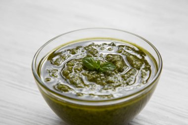 Beyaz ahşap arka planda, yan görünüm taze yapılmış fesleğen pesto kase. Portre.