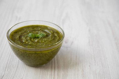 Beyaz ahşap masa, yan görünüm üzerinde taze yapılmış fesleğen pesto kase. Yakın çekim. Kopya alanı.