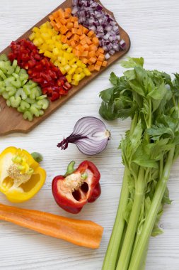 Kesme tahtası üzerinde beyaz ahşap masa, yüksek açılı görünüş olarak düzenlenmiş kıyılmış taze sebzeler (havuç, kereviz, kırmızı soğan, renkli biber). 