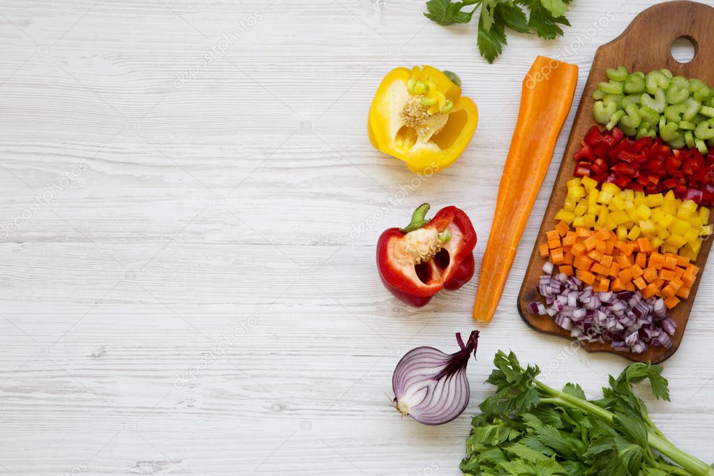 Chopped fresh vegetables (carrot, celery, red onion, peppers) arranged on cutting board on white wooden table, top view. From above, overhead, flat lay. Copy space and text area.