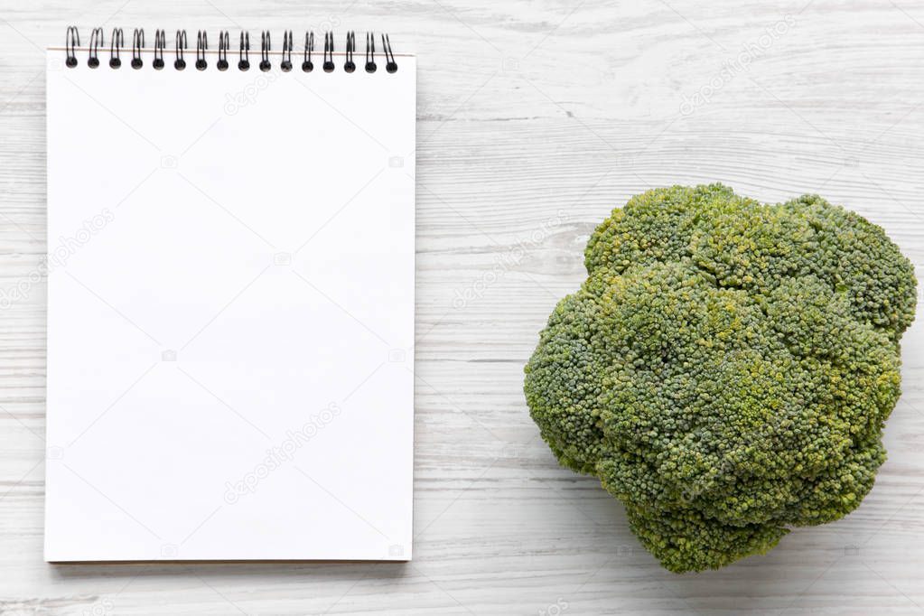 Raw broccoli and blank notepad on white wooden table, overhead view. Space for text.
