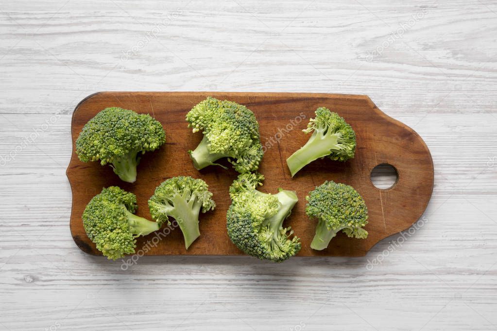 Raw broccoli on rustic cutting board on white wooden background, overhead view. Flat lay, from above. Close-up.