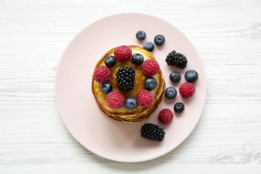 Beyaz ahşap masa, havai görünümü üzerinde pembe bir plaka üzerinde çilek ile krep. Yukarıdan, ana sayfa görünümü.