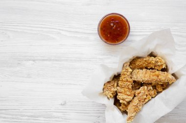 Tavuk şeritler yukarıdan bir beyaz tahta masada tatlı biber soslu kağıt kutusunda görüntüleyin. Düz yatıyordu, en iyi görünüm, ek yükü. Kopya alanı.
