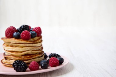 Beyaz ahşap arka plan, yan görünüm üzerinde pembe bir plaka üzerinde çilek ile krep. Kopya alanı.