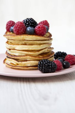 Beyaz ahşap arka plan, yan görünüm üzerinde pembe bir plaka üzerinde çilek ile krep. Yakın çekim.