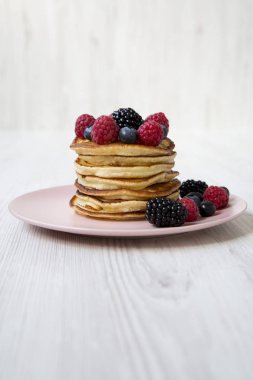 Beyaz ahşap arka plan, yan görünüm üzerinde pembe bir plaka üzerinde meyveleri ile Pancakes. 