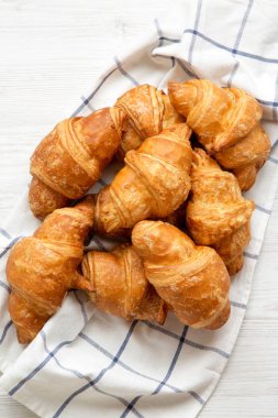 Beyaz ahşap yüzeyde kumaş üzerine taze pişmiş kruvasanlar yukarıdan görüntüleyin. Üstten görünüm, ek yükü. Portre.