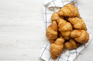 Taze pişmiş kruvasanlar Beyaz ahşap masa, üstten görünüm üzerinde kumaş üzerine. Yukarıdan, tepegöz, düz yatıyordu. Metin için yer.