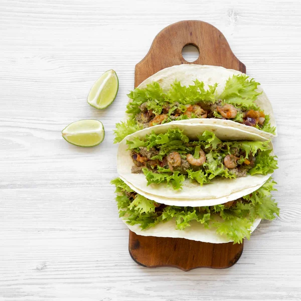 Shrimp tacos on rustic wooden board on white wooden background, overhead view. Flat lay, from above.