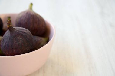 Beyaz ahşap zemin, yan görünüm üzerinde pembe bir kase taze incir. Metin için yer. Seçici odak.