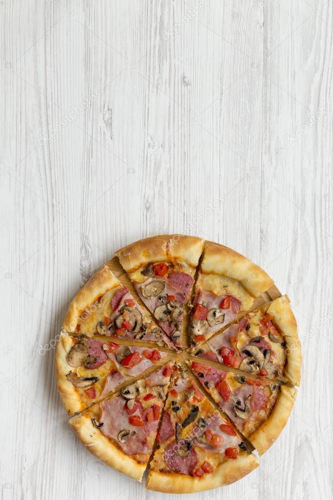 Freshly baked pizza on round bamboo board on white wooden table, top view. Flat lay, overhead, from above. Copy space and text area.