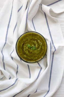 Fesleğen pesto Beyaz ahşap masa, üstten görünüm üzerinde kumaş üzerine kase. Düz, tepegöz, yukarıdan yatıyordu.