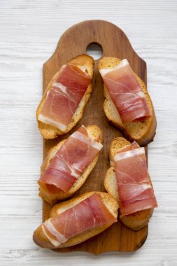 Crostini ile serrano jambonu Beyaz ahşap masa, ahşap tahta üzerinde üst görünüm. Düz, tepegöz, yukarıdan yatıyordu.