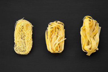 Siyah yüzey, en iyi görünümü üzerinde çeşitli pişmemiş makarna (fettuccine, pappardelle, tagliolini) kümesi. Yakın çekim.