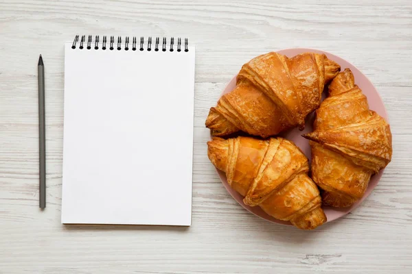 Fresh Croissants Golden Crust Blank Notebook White Wooden Table Overhead — Stock Photo, Image