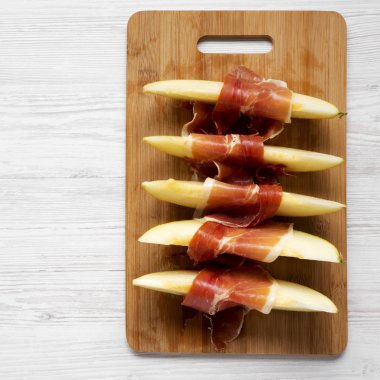 Prosciutto Bambu tahta üzerinde beyaz ahşap bir masa üstten görünüm üzerinde sarılı kavun dilimleri. Yakın çekim. Yukarıdan, tepegöz, düz yatıyordu. 