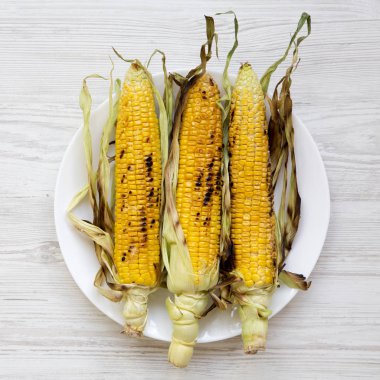 Beyaz tabakta Mısır koçanı Beyaz ahşap zemin üzerinde ek yük ızgara. Yukarıdan, üstten görünüm, düz yatıyordu. Yakın çekim.