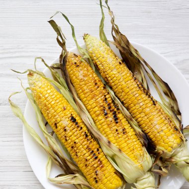 Beyaz ahşap masa, üstten görünüm üzerinde beyaz tabakta üzerinde ızgara Mısır. Yukarıdan, tepegöz, düz yatıyordu. Yakın çekim.