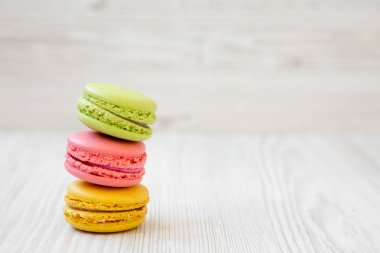 Yan görünümü bir beyaz woodaen arka plan üzerinde renkli macaroons yığını. Kopya alanı.