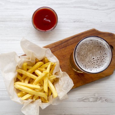 Patates kızartması, ketçap ve bir beyaz tahta masada soğuk bira yukarıdan görüntüleyin. Üstten görünüm, ek yükü. Yakın çekim.