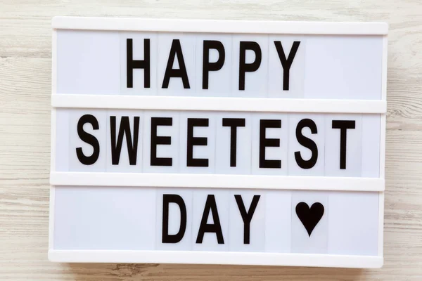 Lightbox with text 'Happy Sweetest Day' word over white wooden background, top view. From above, flat lay, overhead.