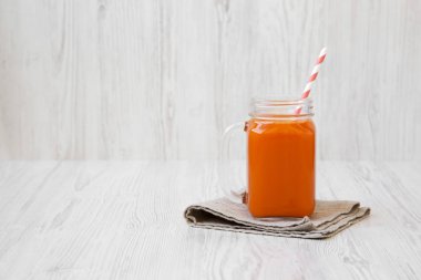 Cam sürahi havuç güler yüzlü beyaz ahşap yüzey, yan görünüm üzerinde. Portre. Metin için yer.