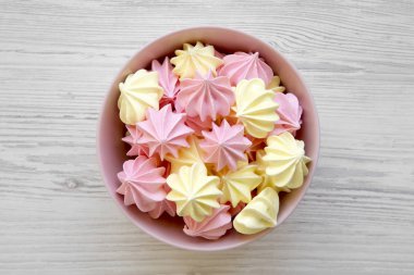 Mini meringues Beyaz ahşap arka plan, üstten görünüm üzerinde pembe bir kase. Düz, tepegöz, yukarıdan yatıyordu.
