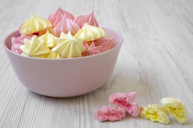 Mini meringues Beyaz ahşap arka plan, yan görünüm üzerinde pembe bir kase. Portre. 