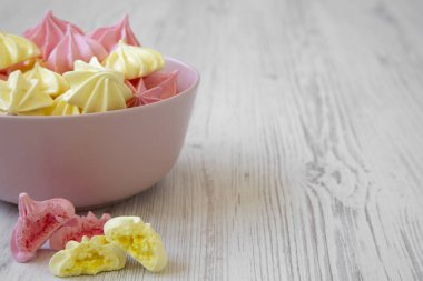 Mini meringues Beyaz ahşap arka plan, yan görünüm üzerinde pembe bir kase. Portre. Kopya alanı.