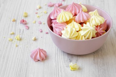 Mini meringues Beyaz ahşap arka plan, yan görünüm üzerinde pembe bir kase. Yakın çekim.