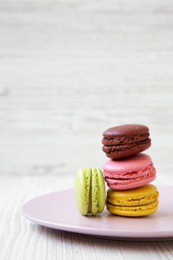 Tatlı ve beyaz ahşap yüzey, yan görünüm üzerinde pembe plaka üzerinde renkli macarons. Yakın çekim. Kopya alanı.
