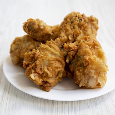 Kızarmış tavuk drumsticks bir beyaz yuvarlak tabak Beyaz ahşap arka plan üzerinde yakın çekim. Yan görünüm.