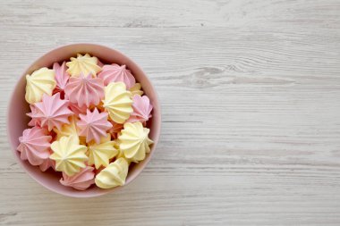 Mini meringues pembe bir kase, üstten görünüm. Düz, tepegöz, yukarıdan yatıyordu. Beyaz ahşap arka plan. Kopya alanı.