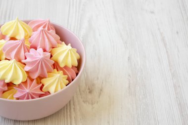 Mini meringues Beyaz ahşap arka plan, yan görünüm üzerinde pembe bir kase. Kopya alanı.