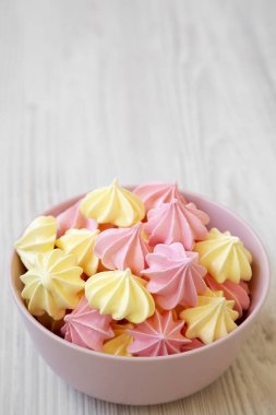 Mini meringues Beyaz ahşap bir masa yan görünüm üzerinde pembe bir kase. Yakın çekim. Kopya alanı.